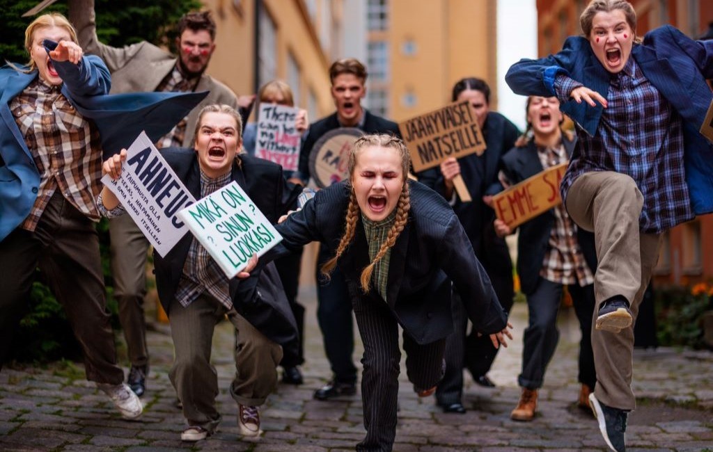 Nuoret näyttelijät juoksevat mielenosoituskyltit kädessä.
