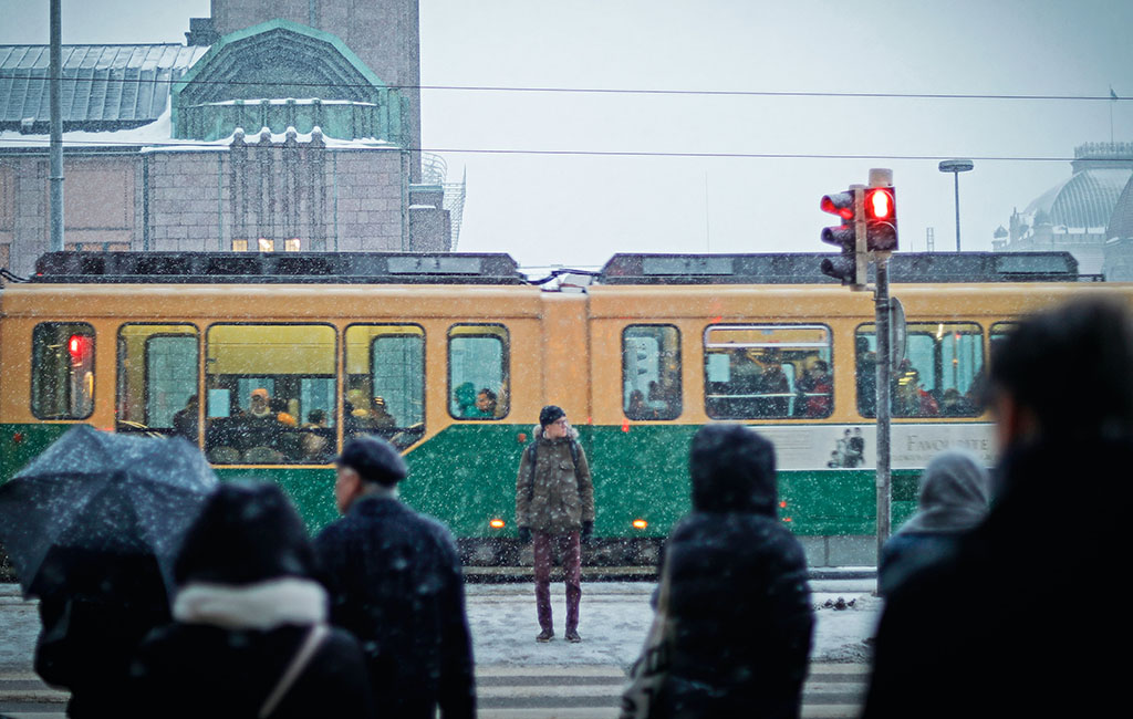 Ihmisiä suojatiellä ja raitiovaunu lumisessa Helsingissä.